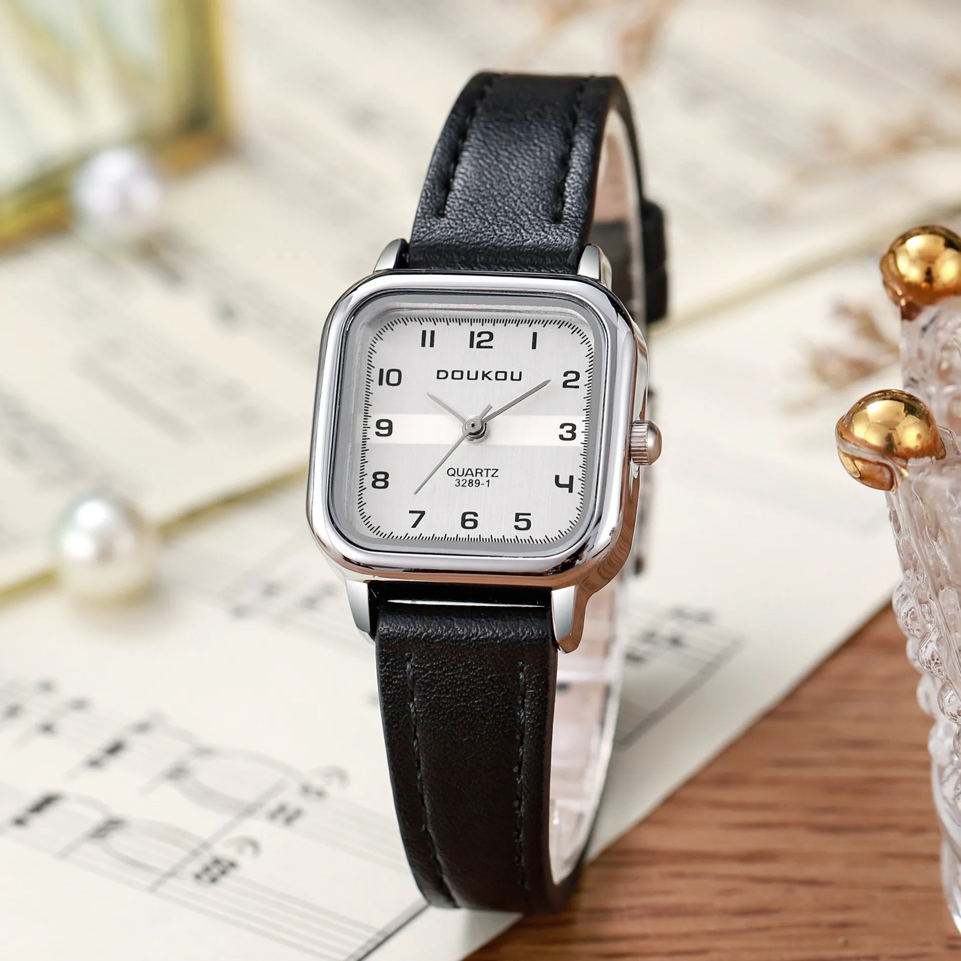 Front view of the square-shaped watch showcasing the clean dial, Arabic numerals, and steel strip band